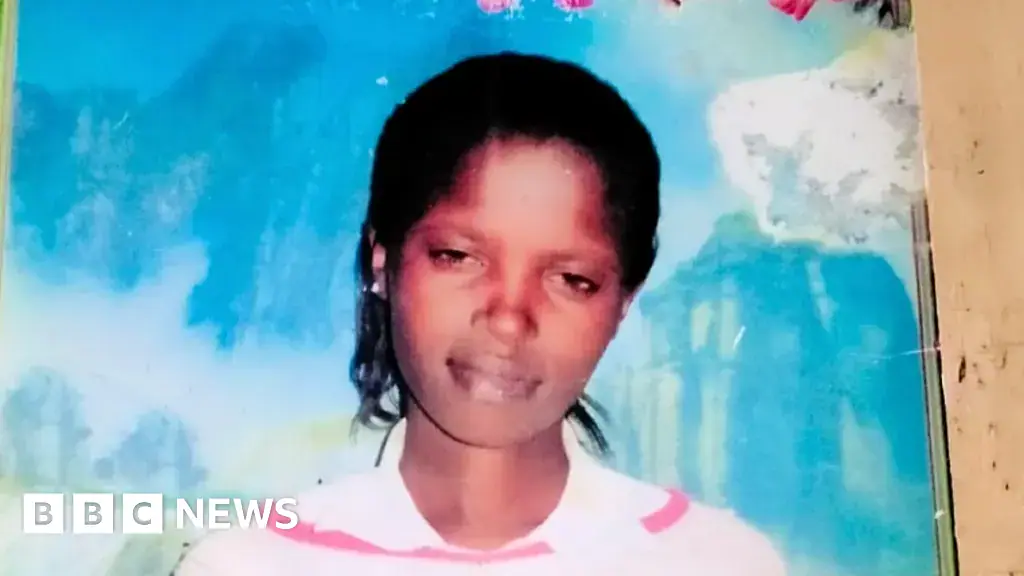 A young woman with dark skin smiling softly in a photo. Behind her is a large blue piece of wall