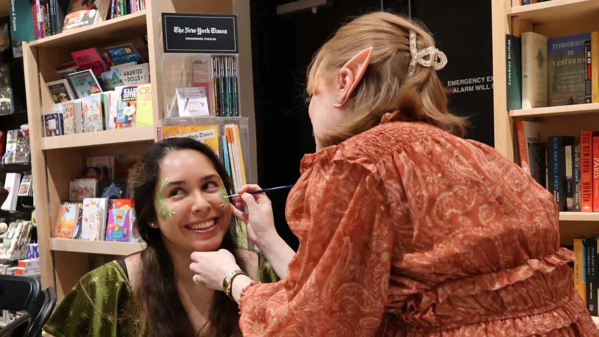 Dalia Luque, left, has her face painted by Amber Lovold, one of the organizers of a midnight release party at Politics and Prose in Washington, D.C. They are celebrating the publication of A Court of Splintered Harmony, the latest installment of Sarah J. Maas' popular romantasy series.