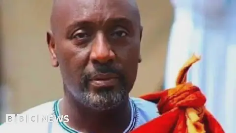 Edward Rukidi Kijanangoma wearing traditional clothing of a white gown with an orange cloth tied around the neck