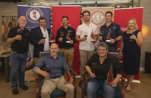 Die wenners in 2026 se Perold Absa Cape Blend-kompetisie. Agter van links is Beyers Truter (voorsitter van die Pinotage Assosiasie), Hennie Kotze (Jakkalsvlei), Andri le Roux (Perdeberg), Luan Steyn (Neethlingshof), Charl Myburgh (Stellenbosch Hills) en Jolene Grobler (Absa). Voor sit Gerhard Swart (Flagstone) en Izéle van Blerk (KWV).
